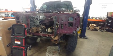 1996 Ford Bronco - Front end of a 1996 Ford Bronco undergoing repairs in a workshop. The vehicle is raised on a lift.
