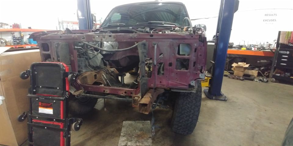 1996 Ford Bronco front end disassembled, showing frame and engine bay components. Vehicle is on a lift in a workshop
