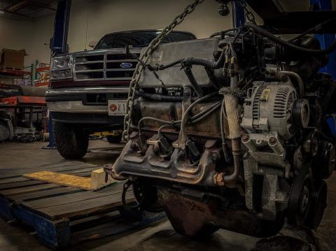 1996 Ford Bronco - A detached engine is hoisted in front of a Ford truck in a workshop setting.