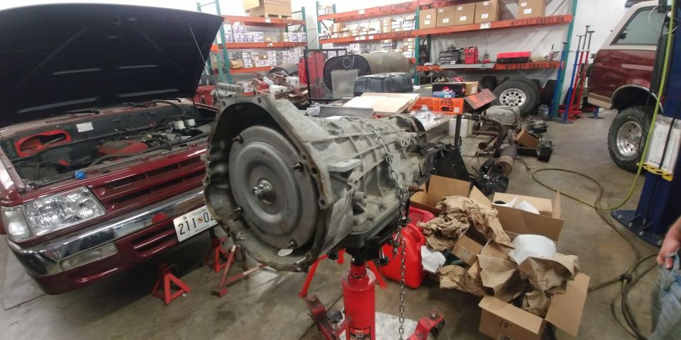 Transmission on stand next to red vehicle with hood open