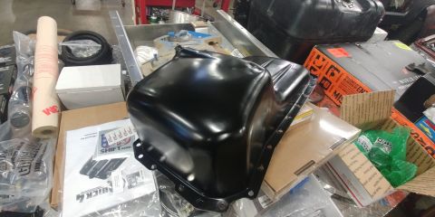 1996 Ford Bronco - A black oil pan is surrounded by various automotive parts and packaging.