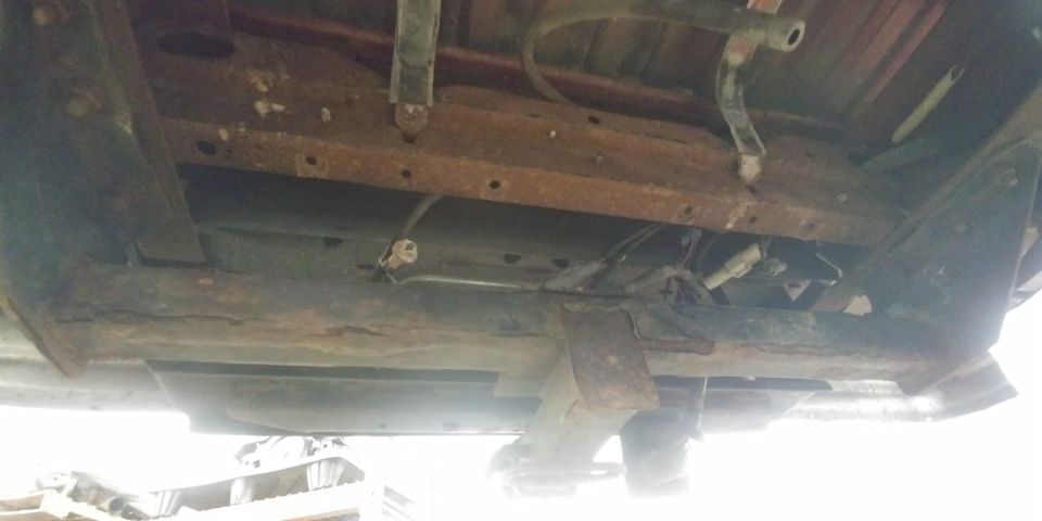 Underside of vehicle frame with extensive rust and suspension components visible