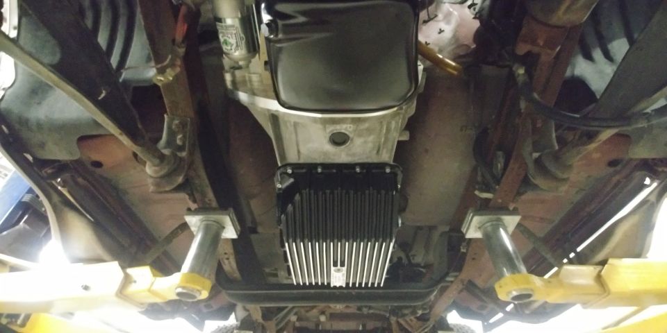 Underside view of a vehicle's transmission and exhaust system, supported by lifts