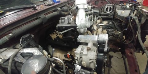 1996 Ford Bronco - Engine bay with a large turbocharger and alternator installed, showing ongoing construction.