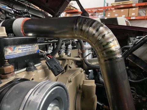 1996 Ford Bronco - Close-up of a custom exhaust pipe installation on an engine, showing engine components and an oil label.