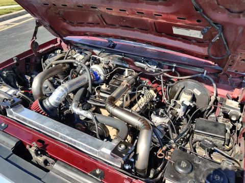 1996 Ford Bronco - Customized engine bay a turbocharger and extensive piping modifications, viewed under the hood of a red vehicle.
