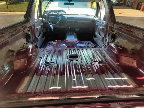 1996 Ford Bronco - The interior of a maroon SUV, stripped down to its metal frame, reveals the dashboard and steering wheel.