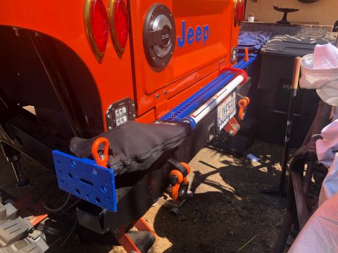 1992 Jeep Wrangler - The rear of an orange Jeep Wrangler is shown with a Hi-Lift jack mounted to the bumper. A blue license plate frame with the text "BOARS NES…