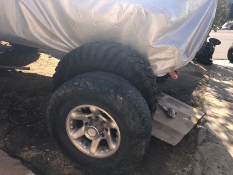 1992 Jeep Wrangler - Two large off-road tires are visible, one stacked on top of the other, with the bottom tire mounted on a silver rim. The tires are partiall…