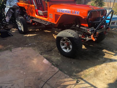 1992 Jeep Wrangler - An orange Jeep Wrangler, nicknamed "General Lee" with blue lettering, is parked outdoors on a dirt and stone surface. The vehicle features…