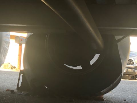 1992 Jeep Wrangler - Underside view of a spare tire mounted underneath a vehicle, possibly a trailer or RV, with a portion of a truck visible in the background.