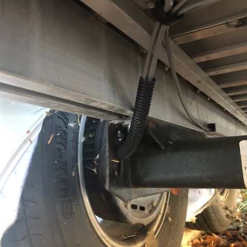 1992 Jeep Wrangler - A close-up view of the undercarriage of a trailer, showing a black corrugated conduit protecting electrical wires attached to the frame nea…