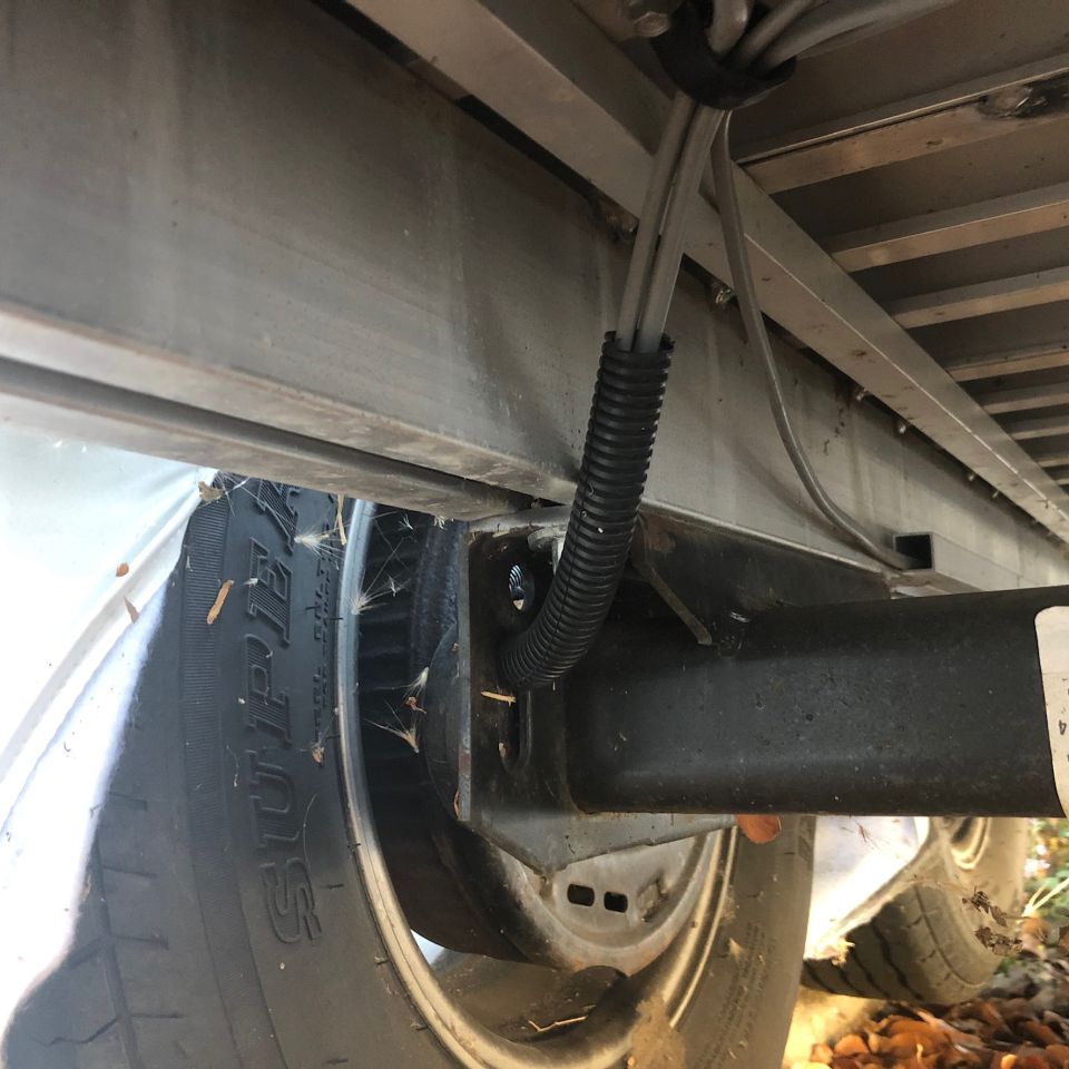Undercarriage of a trailer with electrical conduit and wiring near the wheel.