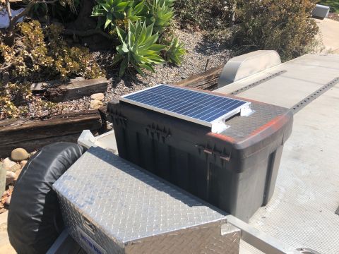 1992 Jeep Wrangler - A small solar panel is mounted on top of a black storage container on a trailer. A spare tire is visible to the left of the container.