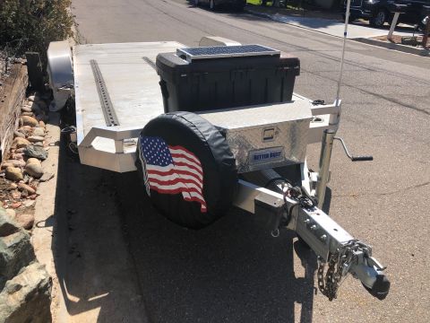 1992 Jeep Wrangler - A utility trailer with a diamond plate toolbox, a black storage box, and a solar panel is parked on an asphalt surface next to a rocky emba…