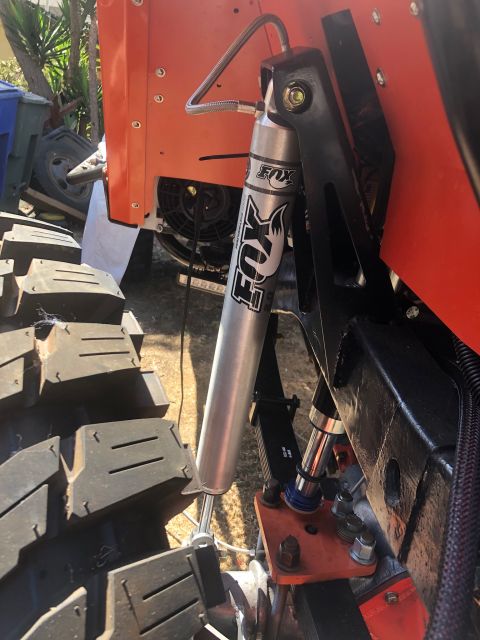 1992 Jeep Wrangler - A close-up view of the suspension system on an orange off-road vehicle, featuring a silver Fox shock absorber mounted to a black bracket an…