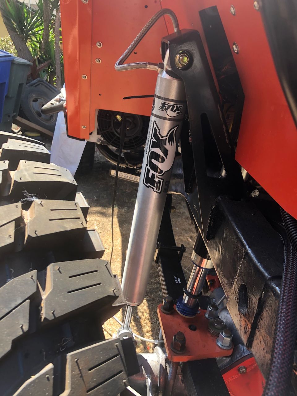 Close-up of Fox shock absorber on an orange off-road vehicle with large tire.