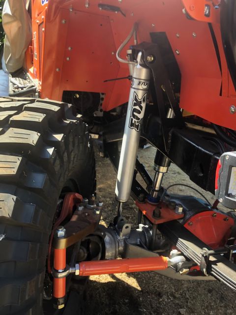 1992 Jeep Wrangler - A close-up view of the suspension system of an orange off-road vehicle, featuring a silver Fox shock absorber and large tires. The vehicle…