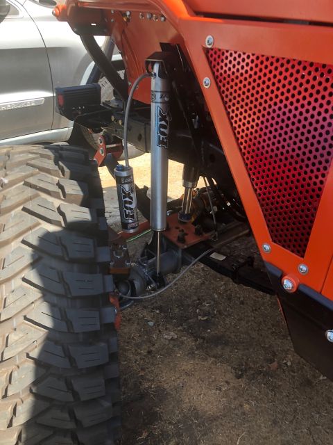 1992 Jeep Wrangler - Close-up of the orange-painted suspension and large off-road tire of a modified Jeep Wrangler. Two silver Fox shock absorbers are visible,…