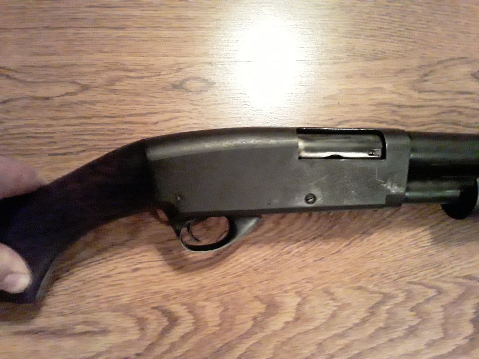 Close-up side view of a dark shotgun on a wooden table.