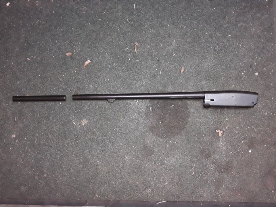 Disassembled firearm barrel and receiver on a dark, textured surface.