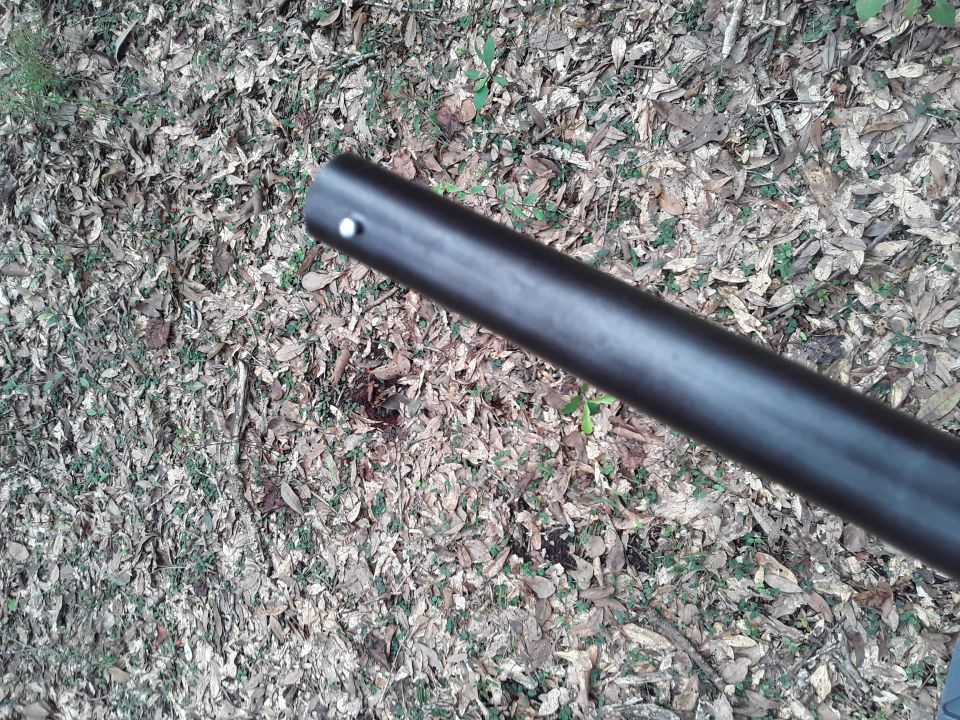 Close-up of a dark barrel pointing towards a leaf-covered forest floor.