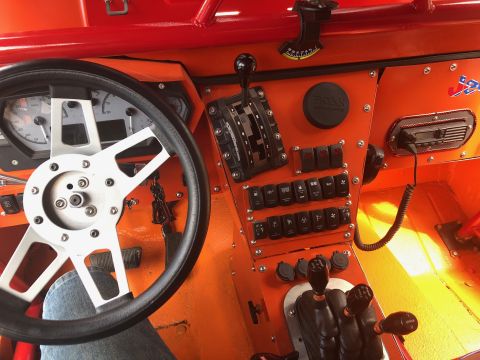 1992 Jeep Wrangler - The interior of a bright orange vehicle shows a steering wheel, dashboard with gauges, and a center console with multiple switches and gear…
