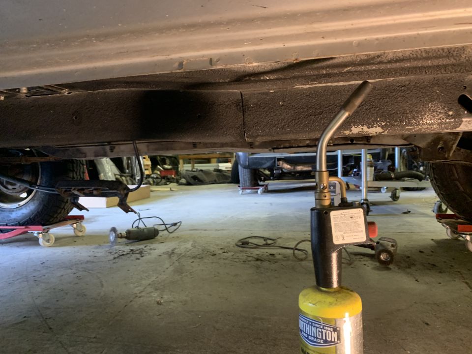 Underside of a Jeep Cherokee with a propane torch in the foreground.
