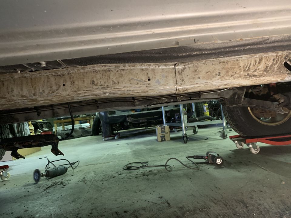Underside of a vehicle frame with tools on the floor, and a tire on a dolly.
