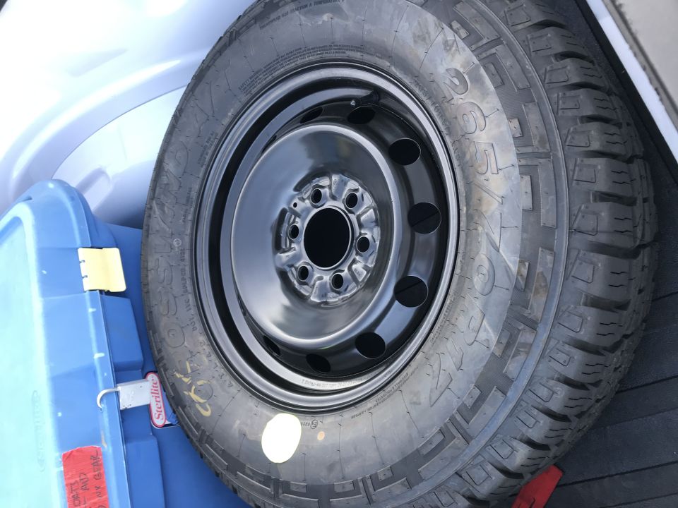Spare tire in trunk next to a blue storage bin. Tire has text and markings on sidewall