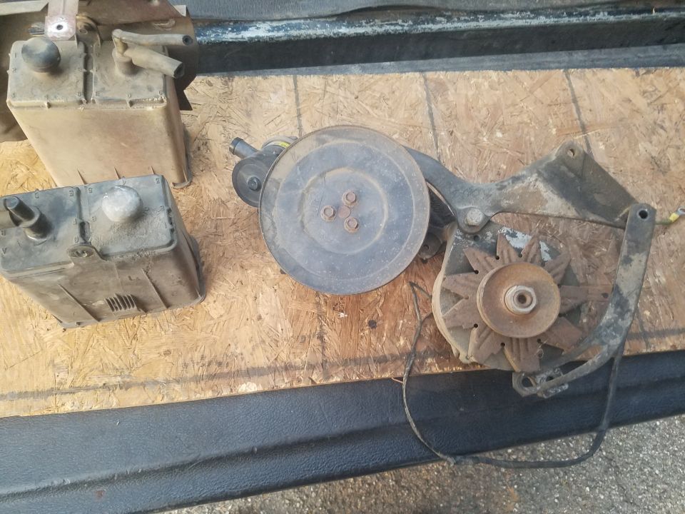 Two plastic containers and a car alternator with pulley system on a wooden surface.