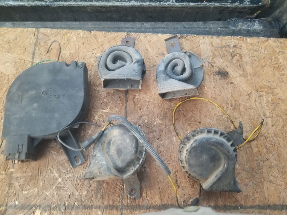 Several old vehicle horns and a black plastic part on a wooden surface.