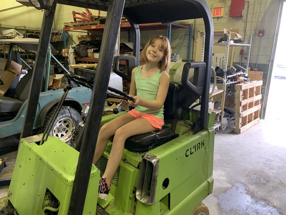Girl sitting in a green Clark forklift, holding the steering wheel.