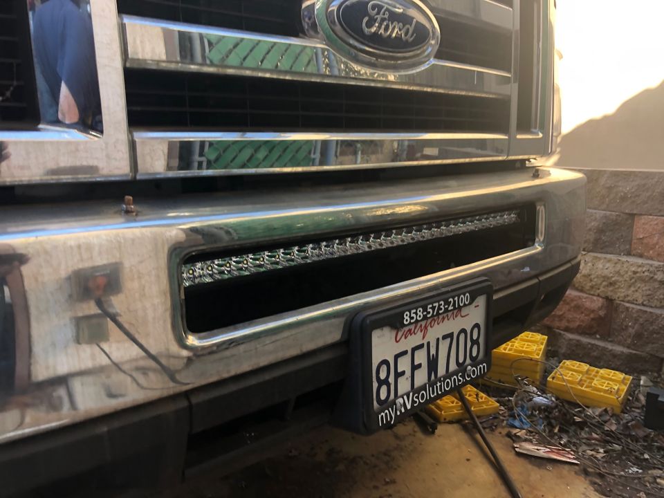 Close-up of a Ford truck's front bumper with a license plate and LED light bar.