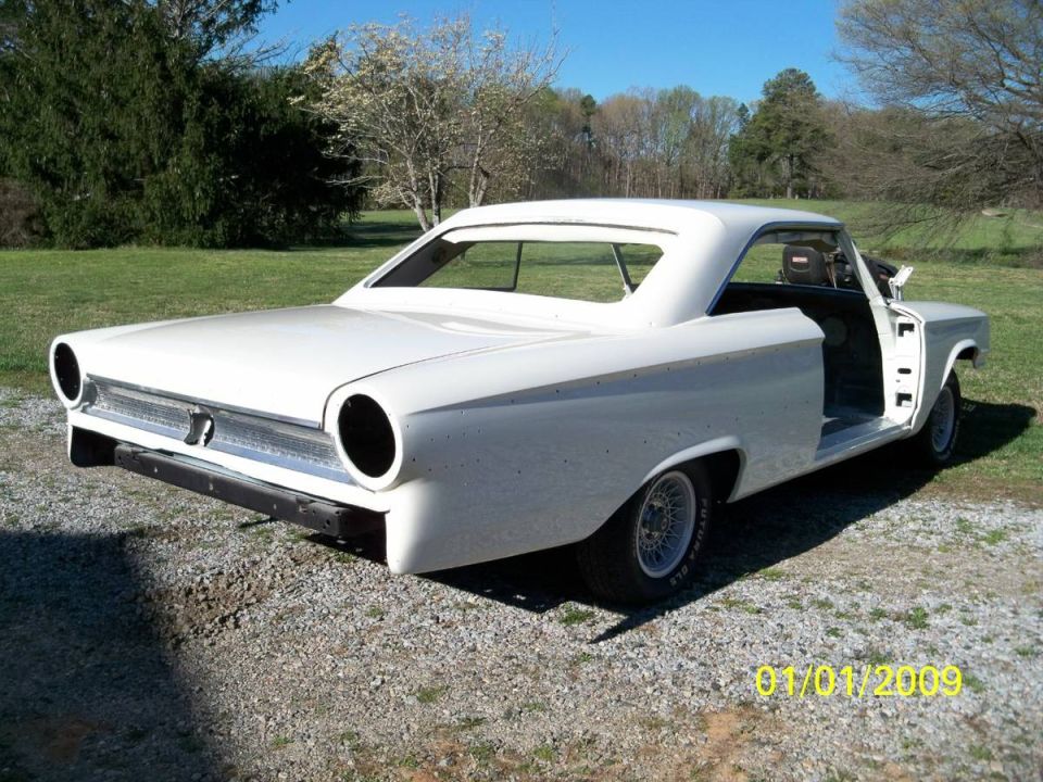 White classic two-door hardtop car with driver's door removed, parked outdoors.