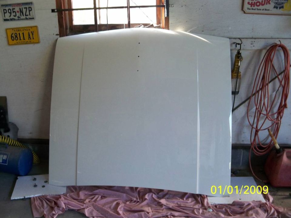 White car hood in a garage with license plates on the wall.