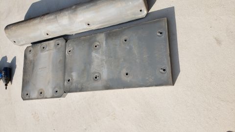 1965 Ford Mustang - Two metal plates and a curved metal bar with visible holes are laid out on a textured surface. A blue and black tool is visible to the left…
