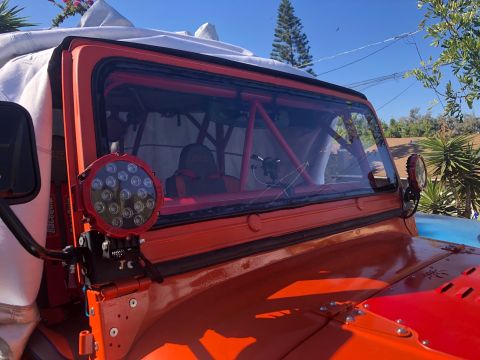 1992 Jeep Wrangler - Close-up view of the front passenger side of an orange Jeep Wrangler, showing a large round LED light mounted to the fender and a portion o…