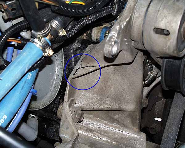 Close-up of a cracked engine casing on a vehicle, with hoses and wiring.