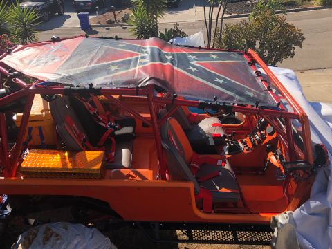 1992 Jeep Wrangler - The interior of an orange off-road vehicle with a roll cage is shown. The roof is covered by a tarp displaying a Confederate flag.