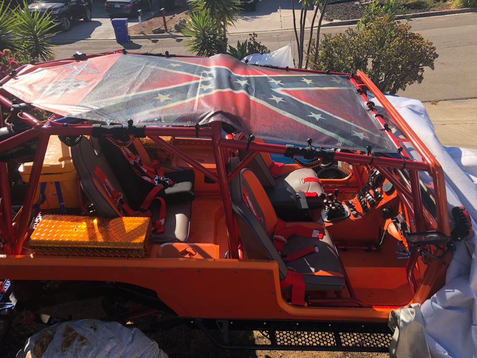 Orange off-road vehicle interior with roll cage and Confederate flag tarp.