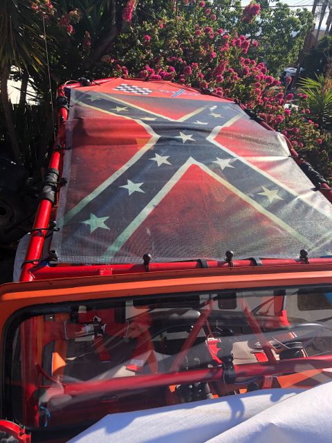 1992 Jeep Wrangler - The roof of an orange Jeep Wrangler is covered with a mesh tarp featuring a large Confederate flag design. The vehicle's interior, includin…