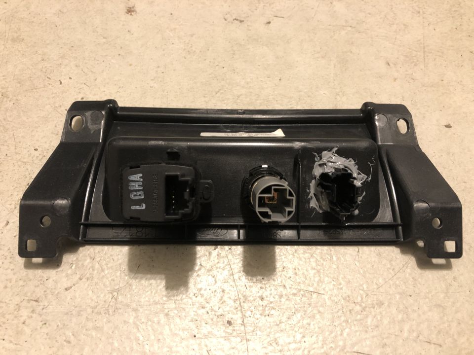 Rear of black Ford plastic trim panel with three switch connectors, one covered in gray sealant