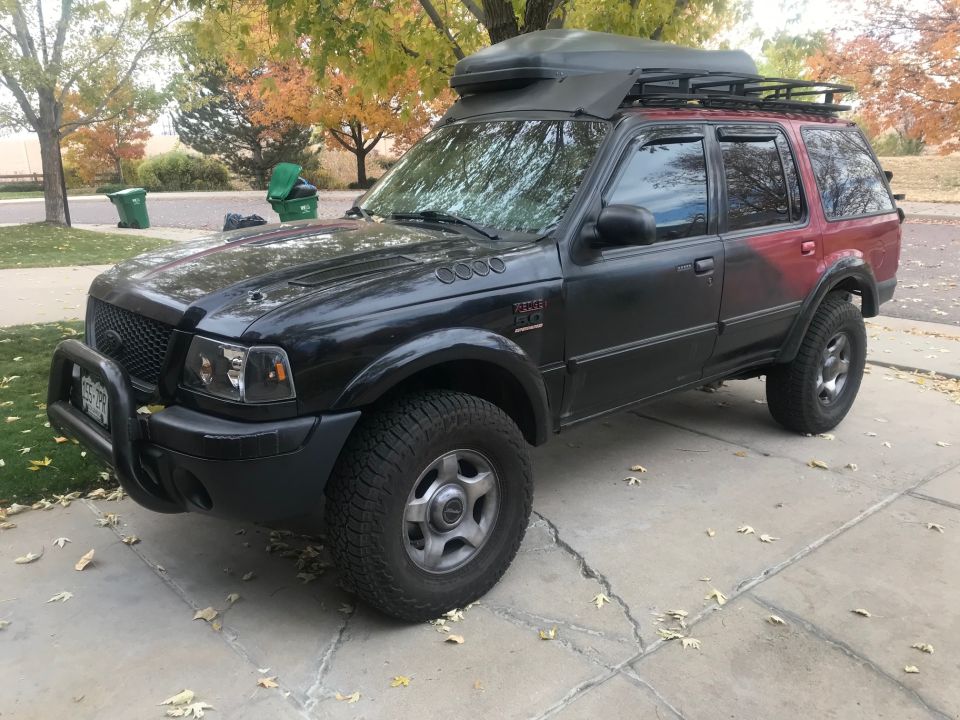 Black Ford Explorer with red accent, roof rack, and cargo box parked on driveway.