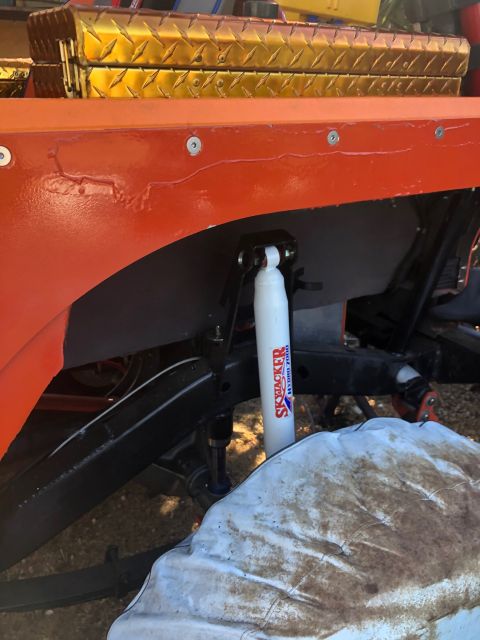 1992 Jeep Wrangler - Close-up of the orange fender and suspension of a Jeep Wrangler, featuring a white Skyjacker shock absorber. A diamond-plated toolbox is vi…