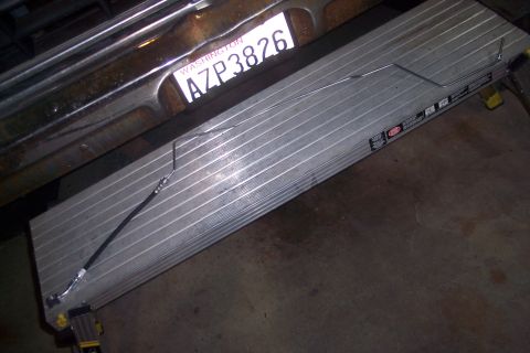1978 Ford Bronco - A close-up view of a metal brake line and hose assembly resting on a silver aluminum ramp, with a Washington license plate reading AZP3826…