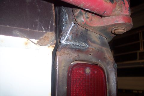 1978 Ford Bronco - A close-up view of the rusted metal frame around a red taillight assembly on a vehicle, showing recent welding repairs near the top.