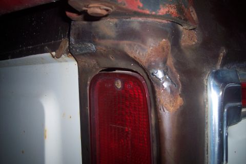 1978 Ford Bronco - A close-up view shows significant rust and welding repairs around the taillight housing of a vehicle. The red taillight lens and a portion…