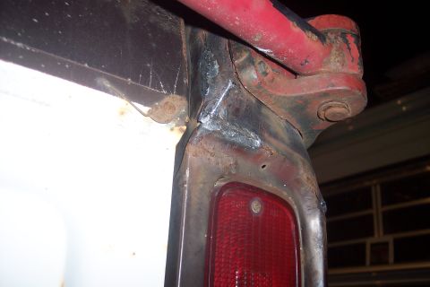 1978 Ford Bronco - A close-up view of the rear corner of a vehicle, showing a red taillight assembly, rusted metal frame with fresh welds, and a red metal bar…