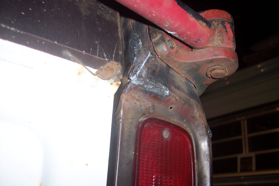 Close-up of rusted vehicle rear corner with red taillight and welded metal.